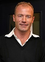 Alan Shearer wearing a black jumper with a white collar visible.