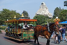 A green and yellow open-air horse-drawn streetcar hitched to a draft horse