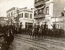 Photographie sépia : des troupes à cheval dans une rue.