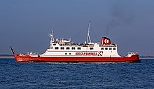 Broadside view of ship, with red hull and white superstructure, steaming right to left