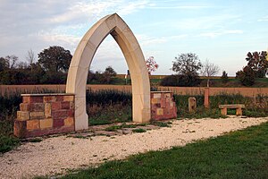 Gotischer Sandsteinbogen als Denkmal am ehemaligen Standort, im Hintergrund der Uferbewuchs des Hainbachs