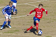 jogador Emil Krafth vestido de vermelho conduzindo a bola com o pé esquerdo em um campo de futebol enquanto existem jogadores de azul correndo atrás.