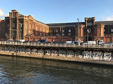 Photographie d'un bâtiment en brique vu depuis la rive d'un canal.