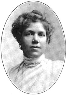 Portrait of a woman with her hair in a top-bun wearing a white lace dress and strands of pearls