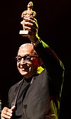 A man in a black shirt is holding an award on his left