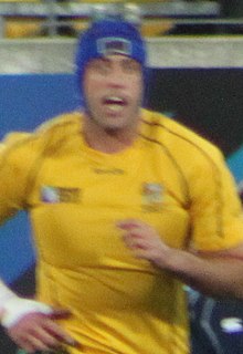 Nathan Sharpe, age 33, wearing yellow rugby kit and blue cap to prevent head injury