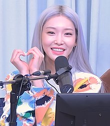 Chung Ha looks at the camera and makes a heart with her hands.