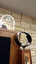 A wooden trophy with a metal oval on top standing in front of a podium, which has a plexiglass trophy on top