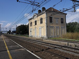 Double-tracked railway line with side platforms and disused two-story building with hipped roof