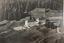 Die Luftaufnahme zeigt das Hochalpine Töchterinstitut Fetan um 1930 mit den beiden Tennisplätzen links vom Gebäude, den beiden Pavillons sowie dem institutseigenen Kräutergarten unterhalb des Gebäudes