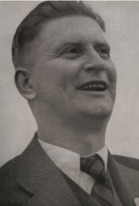 black and white image of Jan Baťa wearing a suit and tie, laughing and looking slightly up and left of camera