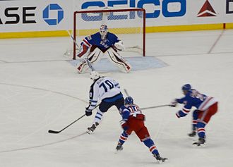 Photographie d'une partie de patinoire avec trois joueurs avec un uniforme de hockey bleu et un avec un uniforme blanc en train de tirer au but.