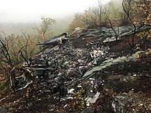Remains of a helicopter, with the environment showing signs of fire. The only part remaining of the aircraft is the tail