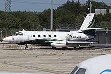 Avion blanc au museau pointu avec deux réacteurs vers l'arrière et des traits verts et dorés le long du fuselage.