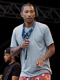 A dark-skinned man wearing a grey short-sleeved shirt is seen looking into the distance during a performance; he is holding a microphone in his hand.