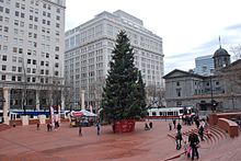 Photograph of a Christmas tree in a public plaza, with buildings in the background