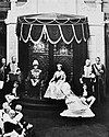A black and white photograph of King George and Queen Elizabeth seated on thrones