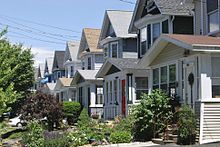 A row of detached wooden gabled houses on the right, all following a similar basic plan but of different colors, with small lawns in front