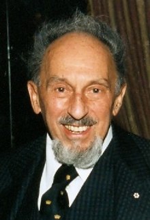 Colour photo of Shumiatcher, grey-haired, balding, with goatee, wearing business jacket and tie, and Order of Canada snowflake lapel pin