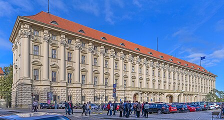 Un bâtiment Renaissance d'une longueur exceptionnelle, de plusieurs étages, au toit de tuiles. Un parking et un groupe de personnes au premier plan. Des bossages en forme de diamants parcours le premier niveau de l'édifice.