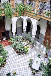 A large, open room that is filled with dining tables and chairs, and plants. The atrium is overlooked from a second story balcony.
