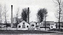 Carte postale ancienne en noir et blanc représentant une usine avec sa cheminée.