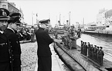 Several people looking at a submarine with its crew on the deck