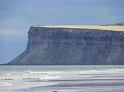 A distant shot of a cliff rising from the sea