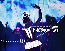 Bright laser lines propagate upward, with a costumed musician standing behind