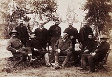 Photographie d'un groupe d'hommes assis dans une forêt.