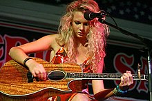 Taylor Swift playing a wooden acoustic guitar made while a large microphone is placed close to her