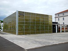 Parvis d'un bâtiment couvert de vitres avec un motif de manuscrit médiéval à l'intérieur des vitres.