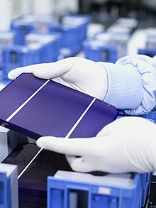 A part of gloved hands are hold a tablet-sized solar cell with three panels.
