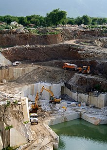 Marble quarry in Jaipur, India. Large rock faces that have been cut to vertical angles, with heavy equipment such as excavators in the picture.