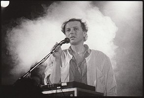 black-and-white image of Luboš Pospíšil standing in front of a control board onstage, holding a microphone, with smoke behind him