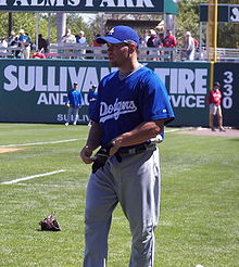 A baseball player plays catch in the infield at Spring Training. He is wearing a blue jersey with the word "Dodgers" in front.