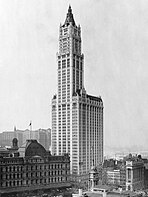 Very tall skyscraper with trees in the foreground and a tall but significantly shorter building to the left