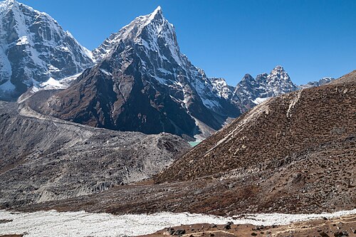 Cholatse is a mountain in the Khumbu region of the Nepalese Himalayas. It has an elevation of 6,440 metres (21,130 ft) above sea level. Cholatse is connected to the slightly higher Taboche by a long ridge. The Chola glacier descends off the east face. A lake is located to the east, which gave the mountain its name – in Tibetan, cho means 'lake', la means 'pass', and tse means 'peak'. Cholatse was first climbed via the southwest ridge in 1982. The north and east faces of the mountain can be seen from Dughla, on the trail to the Everest base camp. This photograph of Cholatse was taken from the east, near Dughla, with a small section of Chola Lake visible in the centre of the image. The terminal moraine of the glacier can be seen in the foreground.