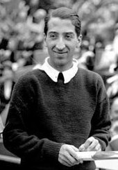 A black-haired man in a white shirt and a black sweater poses for the camera