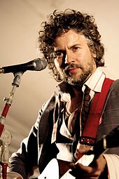 Bearded, curly haired man playing a guitar onstage