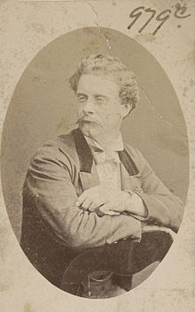 Portrait of Henri with waxed moustache, sitting backwards on a chair, 3/4 to camera, wearing a formal jacket and white bowtie.