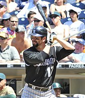 Todd Helton, wearing a black baseball batting helmet and black baseball uniform with the words COLORADO across, holds his bat during an at bat