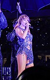 Taylor Swift in a sparkling purple dress performing a chair dance choreography onstage