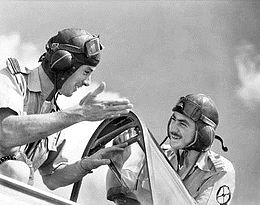 Two men in flying goggles talking beside an aircraft cockpit.