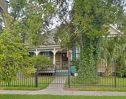 a house with detailed porch is seen from behind gate through trees
