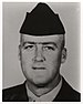 Head of a white man wearing a garrison cap and a dark military jacket over a light-colored shirt.