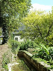 Photographie en couleurs d'un bâtiment partiellement masqué par des arbres avec un petit canal rempli d'eau.