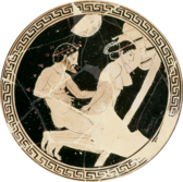 Interior of a Greek cup. The cup is black, with a white image of a woman on her knees and a man kneeing behind her; she is reaching behind her, grasping his penis.