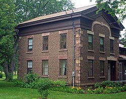 A two-story brown house made of small stones in rows. There are two small satellite dishes on top.