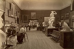 A sepia-toned photograph shows women seated at easels painting copies of the framed paintings on display in a gallery with a high ceiling. In the centre of the room plaster casts of classical Greek statues are displayed on a high plinth.